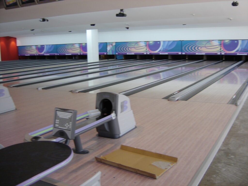 This image showcases a state-of-the-art bowling alley with a visually striking interior. The scene features multiple bowling lanes illuminated by vibrant LED displays that create a captivating and immersive environment. The sleek, polished lanes and the presence of bowling equipment suggest this is a high-quality facility designed to provide an engaging and enjoyable bowling experience for players.